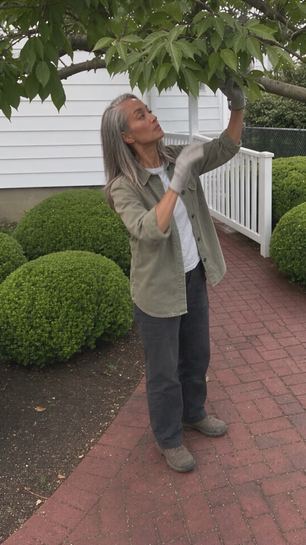 Woman using the Standby 6-inch cordless mini chainsaw one-handed to cut a branch over a walkway, then showing the complete kit in its case